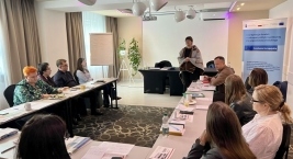 Ludzie siedzą przy stołach w pomieszczeniu, tworząc atmosferę spotkania i interakcji