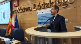 Mężczyzna w eleganckim garniturze wygłasza prezentację przy podium.  