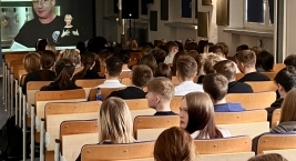 Uczniowie siedzący w sali wykładowej oglądają materiał wideo wyświetlany na ekranie podczas spotkania informacyjnego.