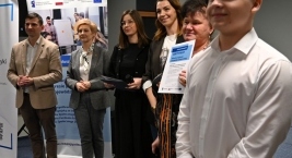 Uczestnicy i organizatorzy wydarzenia stoją razem, jedna z osób trzyma certyfikat „szkoły przyjaznej ekonomii społecznej”